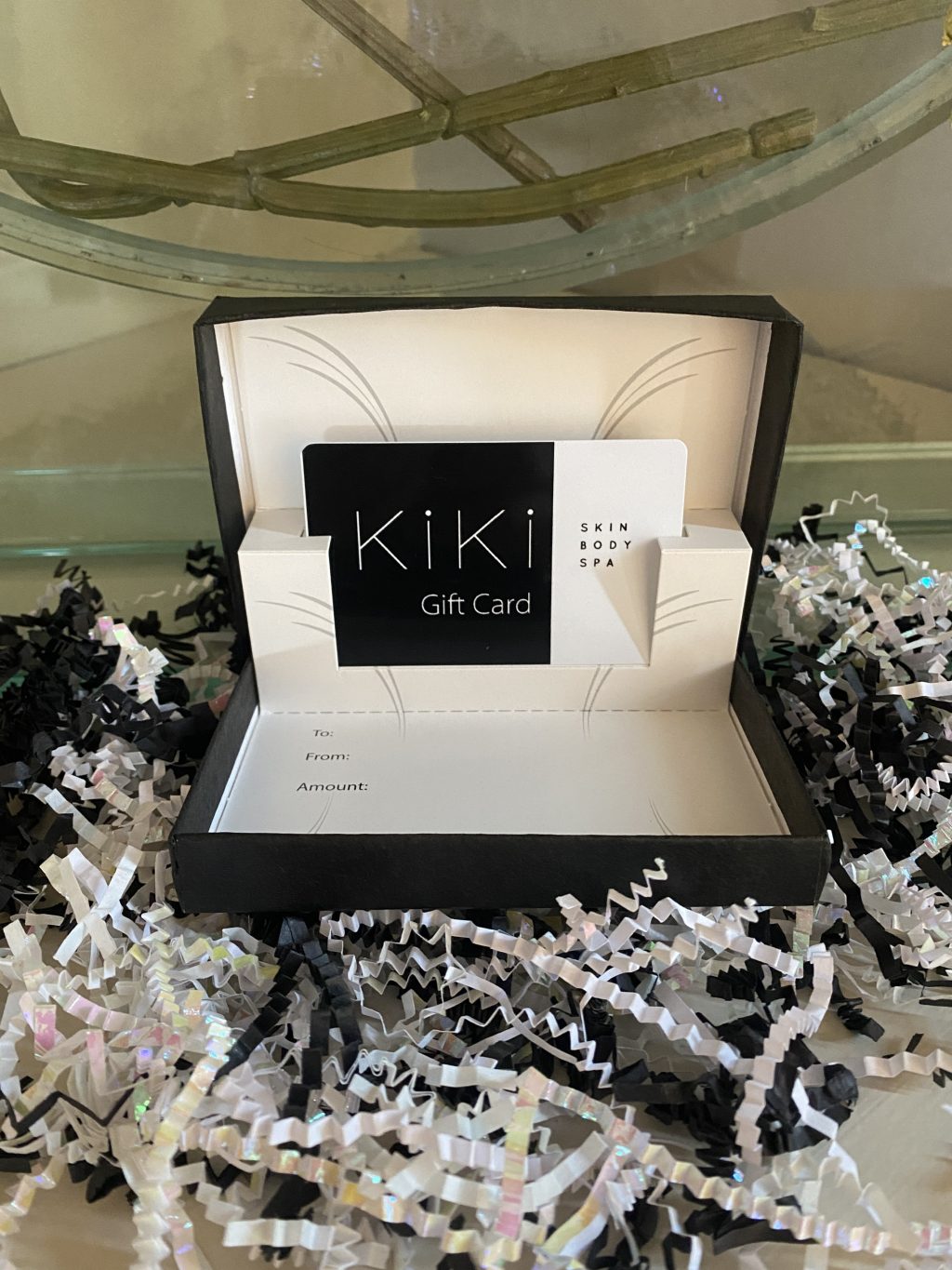 Kiki Kosmetiks gift card in a box surrounded by black and white crimped shredded papers