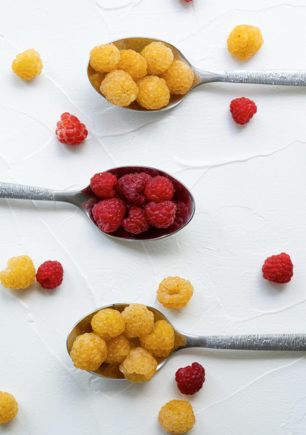 Premium golden and red raspberries displayed on measuring spoons, ideal for food service suppliers and wholesale food distributors.