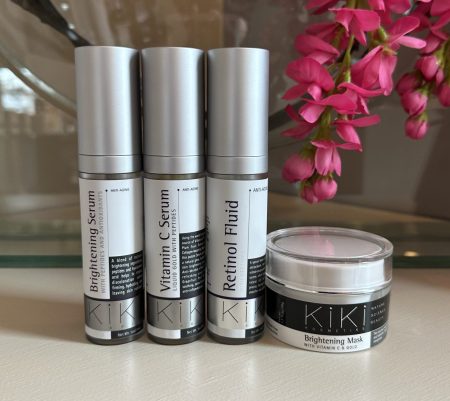 KIKI skincare collection featuring brightening serum, vitamin C serum, retinol fluid, and brightening mask with anti-aging benefits displayed with pink flowers.