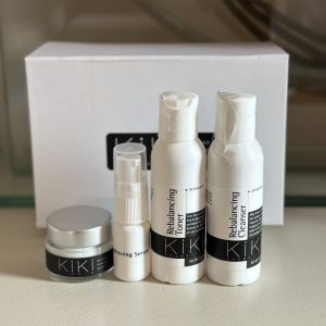 Travel size KiKi Kosmetiks products including cleanser, toner, serum, and moisturizer in white bottles with black labels, displayed with white packaging box.