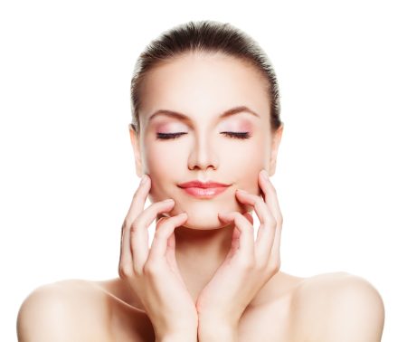Woman with eyes closed and hands gently touching her face, showing healthy glowing skin